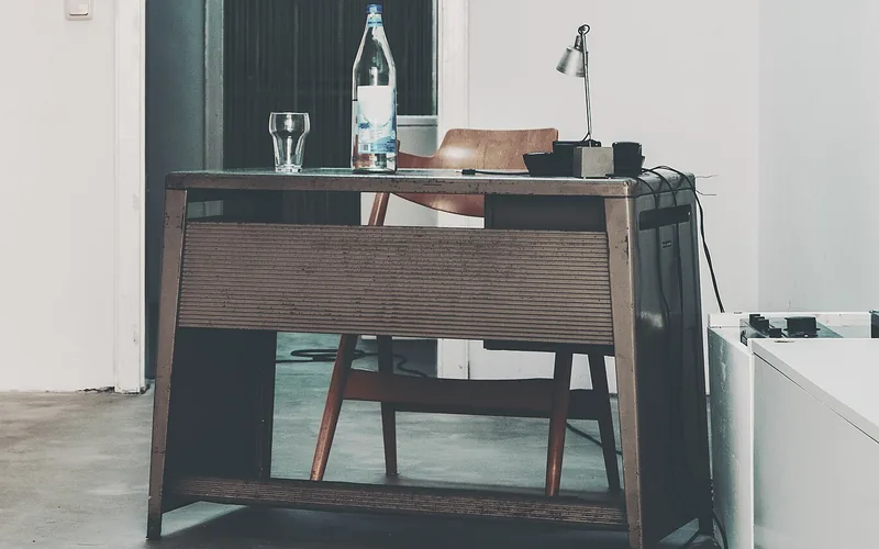 Alter Schreibtisch mit Tischlampe, Wasserflasche und Holzstuhl