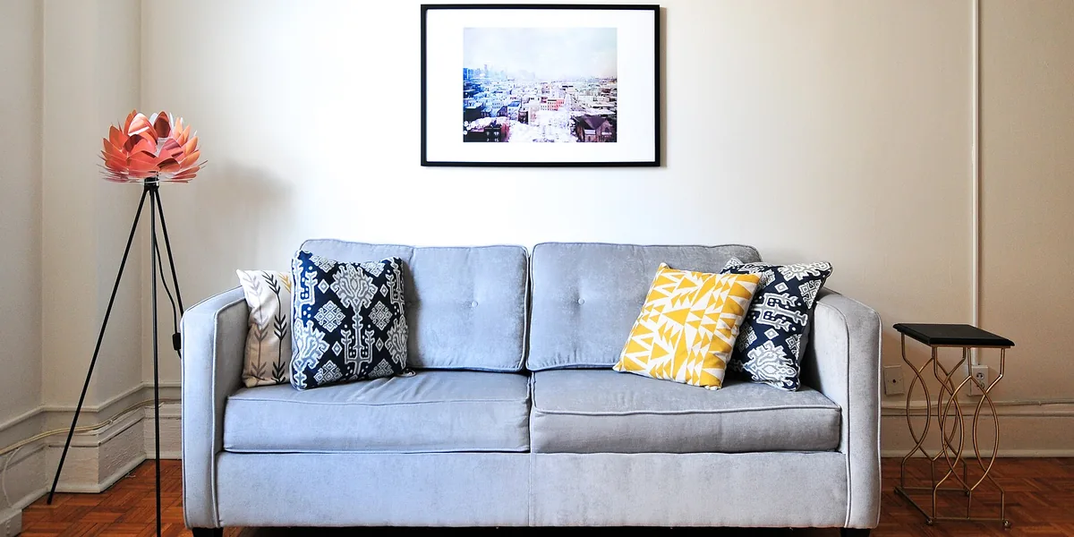 Hellblaues Sofa mit Kissen, Lampe mit Blütenschirm und gerahmtem Bild